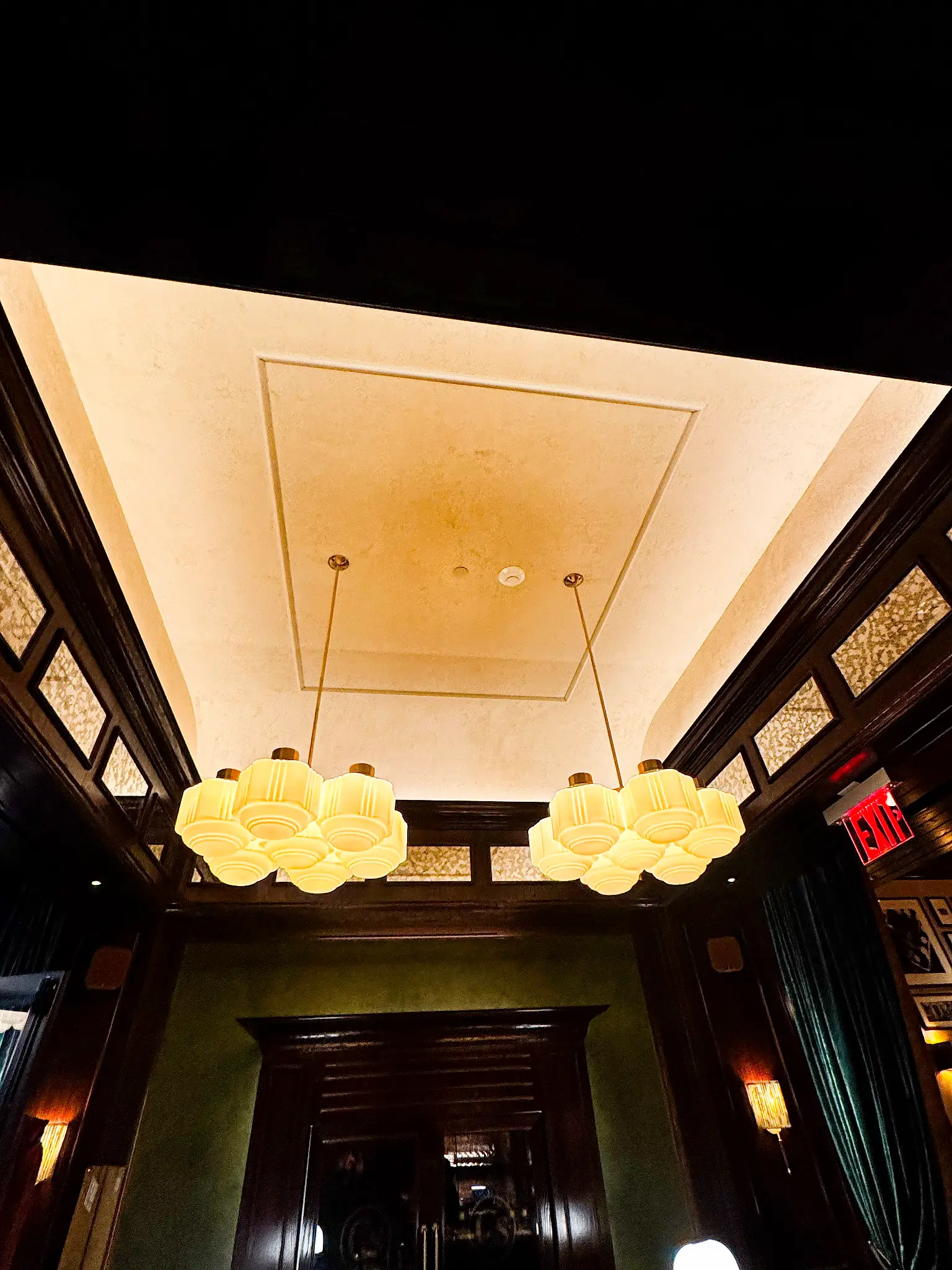 Carversteak NYC — entry corridor in deep bronze plaster beneath twin art deco chandeliers