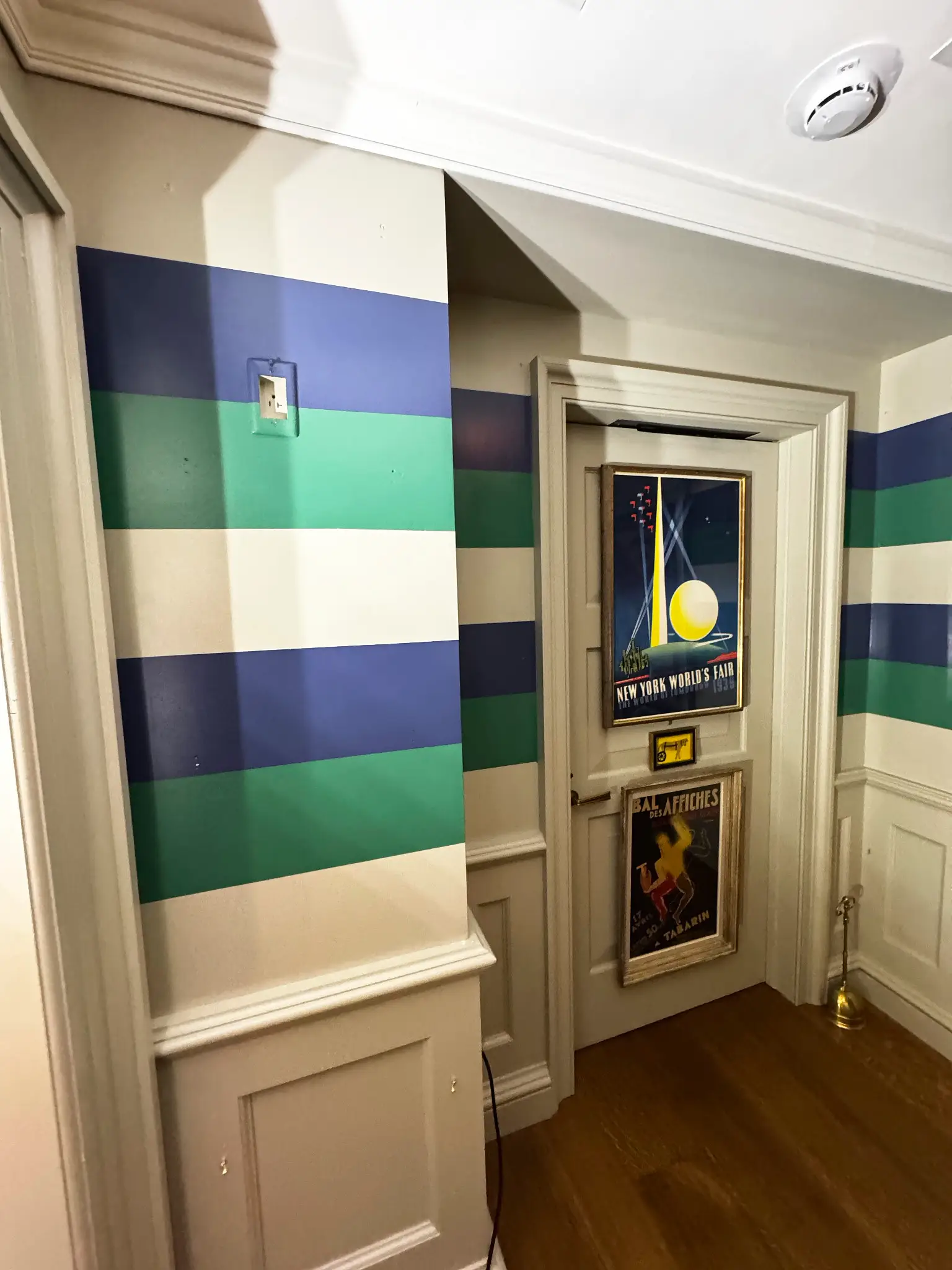Maxime's — corridor view toward a doorway hung with vintage travel posters